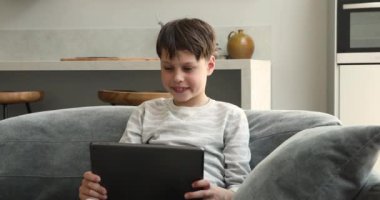 Çocuk elinde tablet, video oyunu oynuyor. Evdeki kanepede otur.