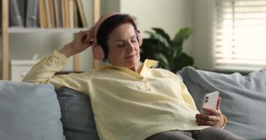 Serene yaşlı kadın kulaklık takıyor. Akıllı telefonu tutuyor. Sakin müzik dinliyor.