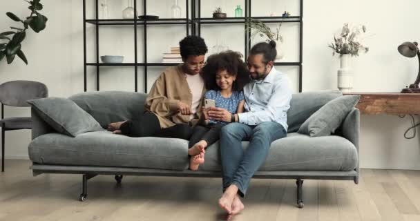 Afrikaans paar en dochter ontspannen op de bank met behulp van moderne smartphone — Stockvideo