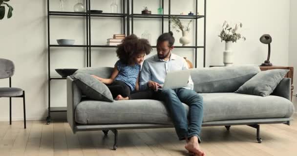 Afrykański tata i córeczka spoczywają na kanapie za pomocą laptopa — Wideo stockowe