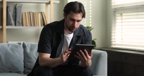 Handsome bearded guy sit on sofa with digital table — Stockvideo