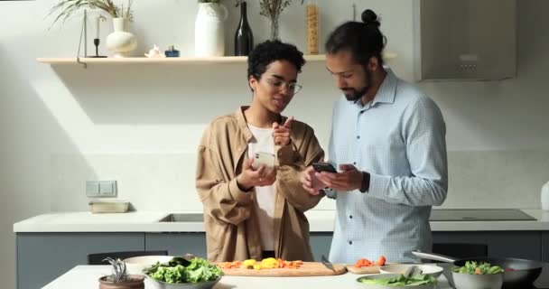 Afrikansk par ved hjælp af smartphones taler i køkkenet, mens madlavning middag – Stock-video
