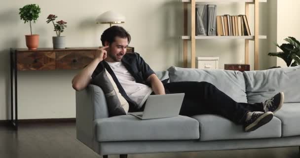 Joven hombre guapo relajante en el sofá acogedor con netbook — Vídeo de stock