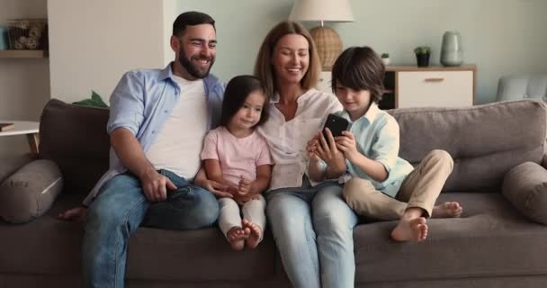 Couple with children sit on sofa enjoy shopping using smartphone — Stockvideo