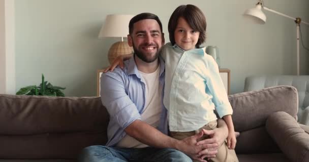 Feliz joven padre sentarse en sofá abrazo con pequeño hijo — Vídeos de Stock