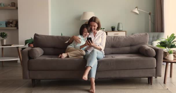 Amigable madre soltera pequeño hijo abrazo en sofá celebración de teléfono — Vídeos de Stock