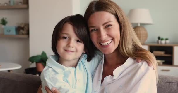 Liefdevolle jonge moeder zitten op bank omarmen voorschoolse leeftijd zoon — Stockvideo