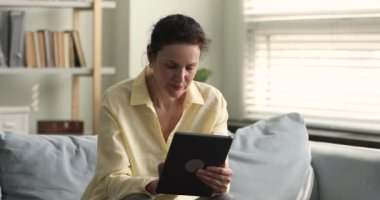 Çekici, olgun bir kadın dijital tablet cihazıyla kanepeye oturur.