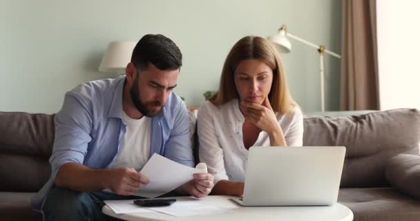 Pareja joven comparar documentos en papel e información en línea sobre el ordenador portátil — Vídeos de Stock