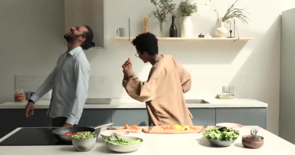 Happy African couple dance in kitchen while cooking vegetable salad — Stock Video