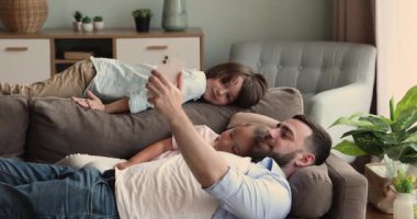 Baba ve çocuklar kanepede uzanıp telefonda çizgi film izlerler.