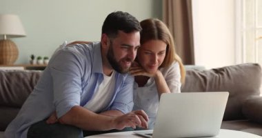 Gülümseyen genç aile dizüstü bilgisayar ekranından önce koltukta dinleniyor.