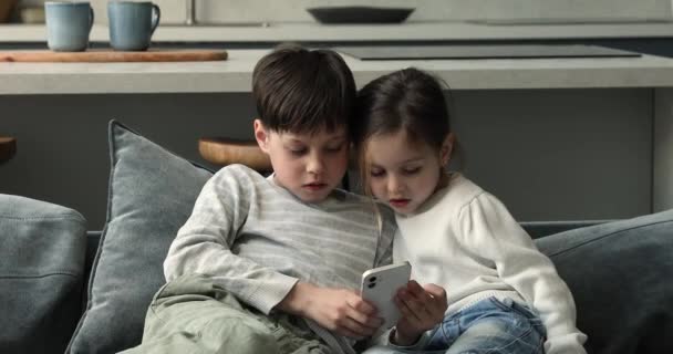 Küçük kız ve oğlan akıllı telefonuyla kanepede oturur. — Stok video