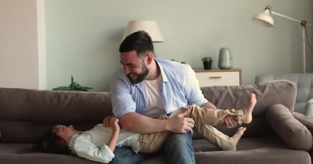 Lachende vader zitten op de bank kietelen gooien opgewonden kleine zoon — Stockvideo