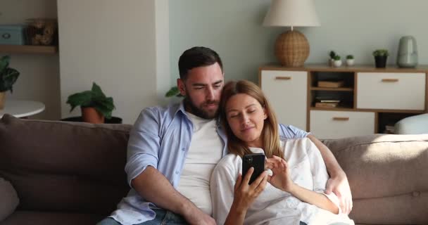 Young husband resting with beloved wife watching video on cellphone — 图库视频影像