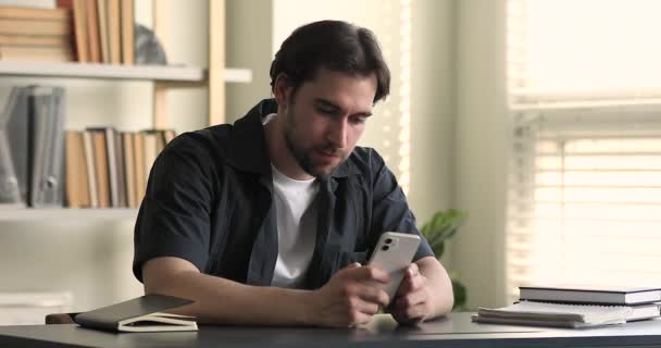 Hombre joven usando teléfono inteligente sonrisa compartir mensajes sentarse en el escritorio — Vídeo de stock