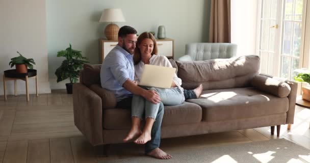 Bonding jovens cônjuges abraçar no sofá olhar na tela do laptop — Vídeo de Stock