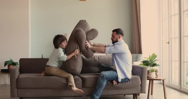 Радісний молодий тато грає подушку боротися на дивані з сином — стокове відео