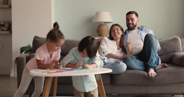Děti dcera syn kreslit náčrty, zatímco rodiče relaxovat na pohovce — Stock video