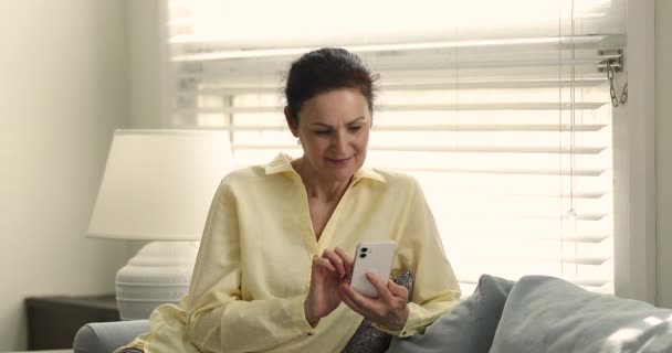 Older woman use smartphone swipe news feed, choose online goods — стоковое видео