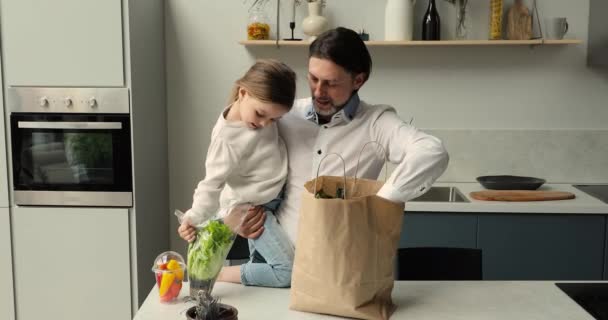 Тато і дочка розпаковують свіжі натуральні овочі з паперового пакету — стокове відео