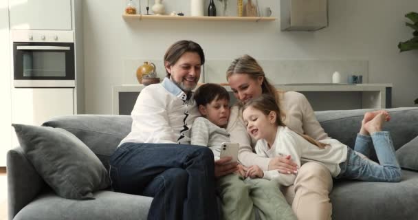 Couple and children relaxing on sofa have fun using cellphone — 图库视频影像