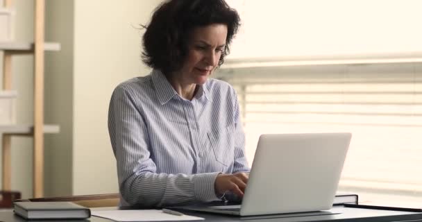 年配の実業家は、ノートパソコンを使用して机のテキストメッセージに座る、メモを取る — ストック動画