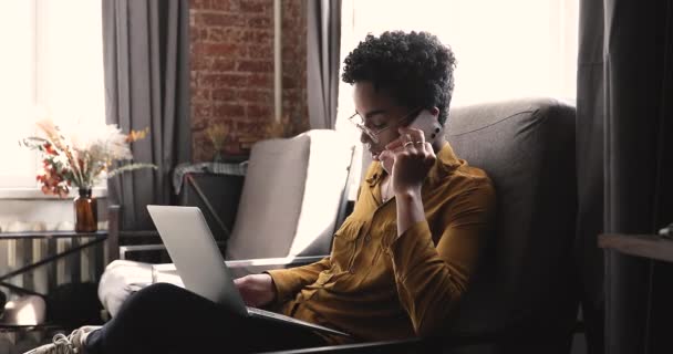 Afrikai nő beszél okostelefonon vezeték nélküli számítógép ölében — Stock videók