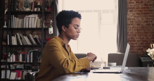 Afrikansk kvinna sitter vid skrivbordet och jobbar på laptop, gör pappersarbete — Stockvideo