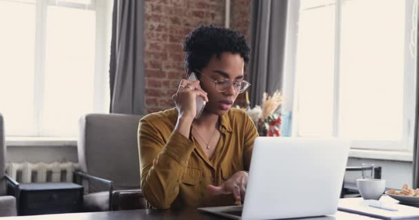 Businesswoman sit at table text on laptop talking on smartphone — Stock Video