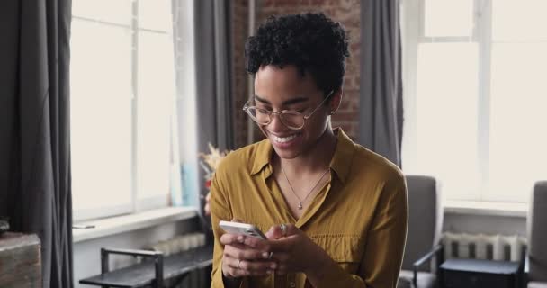 Young African woman in glasses holds smart phone chatting online — ストック動画