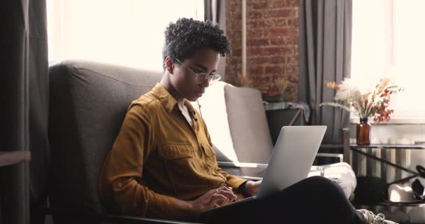 Serious African woman working on laptop while sit on armchair — Stock Video