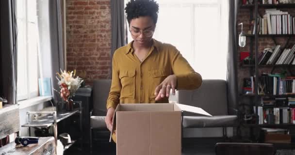 Attractive young African woman unpack parcel with ordered books online — стокове відео