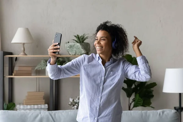 Happy african american woman in headphones dancing at home. — стокове фото