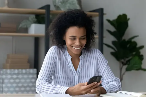 Sourire jeune femme africaine en utilisant un téléphone portable dans le bureau. — Photo