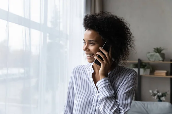 Dreamy happy young african woman holding phone call conversation. — Stock Photo, Image