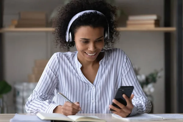 Smiling young african american woman in headphones holding telephone. — Stock Photo, Image