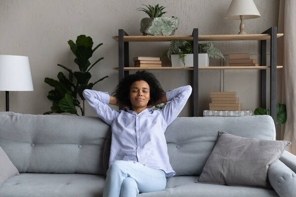 Счастливая молодая африканская женщина отдыхает на уютном диване.