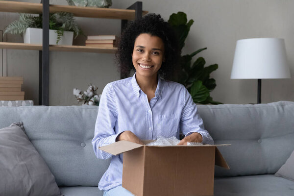 Smiling young african american woman unpacking carton box.