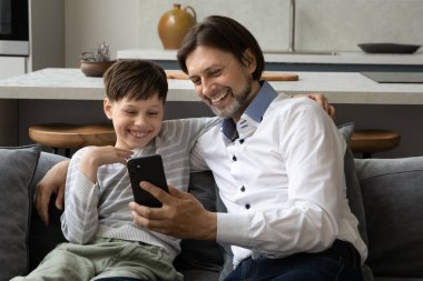 Mutlu baba ve neşeli genç çocuk akıllı telefonu birlikte kullanıyor, paylaşıyor.