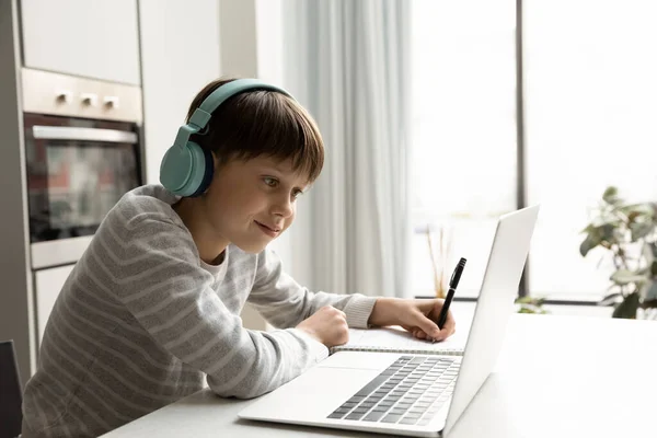 Glimlachende tiener schoolkind in draadloze hoofdtelefoon studeren thuis — Stockfoto