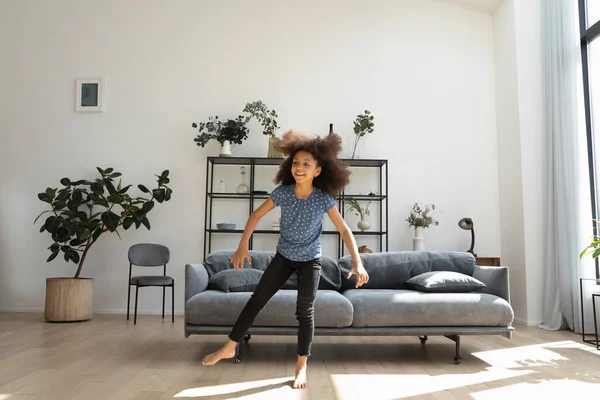 Cheerful cute African American girl dancing to music at home — стокове фото