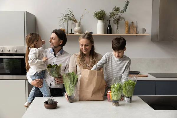 Happy couple of parents and kids unpacking grocery bag — стоковое фото