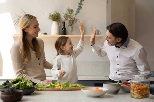 Excited cheerful daughter girl helping parents to cook dinner — стоковое фото