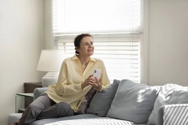Happy dreamy old woman using cellphone at home. — Stock Photo, Image