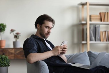 Evde cep telefonu kullanan mutlu ve rahat genç bir adam..