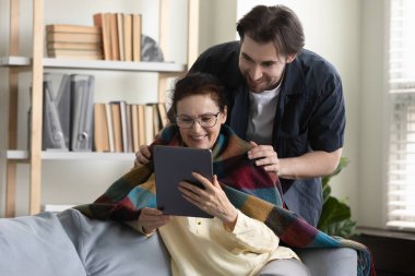Mutlu yaşlı kadın tablet kullanıyor, ilgili oğluyla vakit geçiriyor..