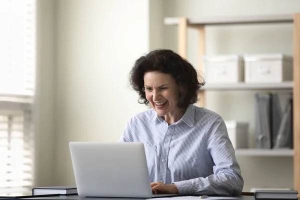 Mujer de mediana edad alegre mirando la pantalla del ordenador portátil. —  Fotos de Stock