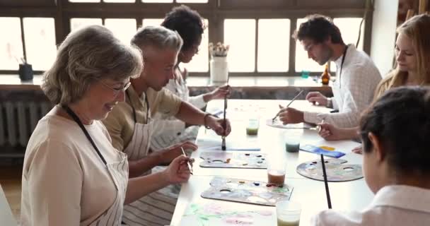 Mujer de mediana edad profesora dar clase de pintura a diversos jóvenes — Vídeo de stock