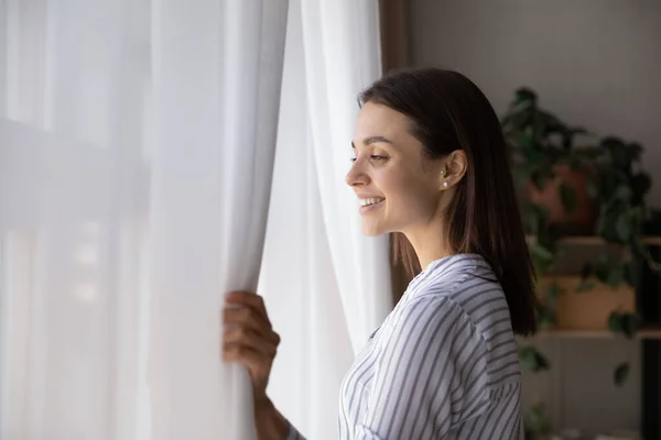 Gelukkige jonge vrouw kijken uit raam thuis — Stockfoto